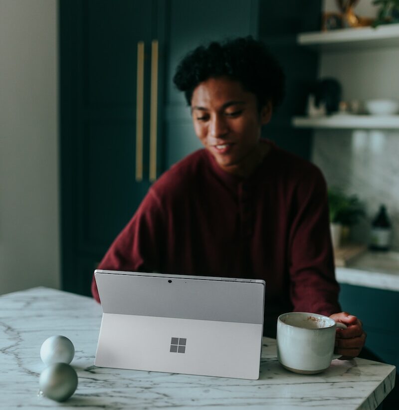 Man sitting at kitchen table watching something on his Surface laptop drinking coffee